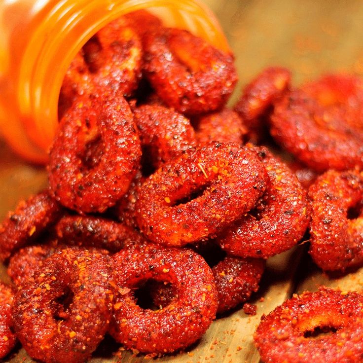 a pile of red food sitting on top of a wooden table next to a bottle