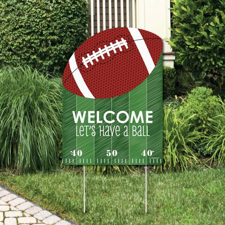 a welcome sign with a football on it in front of some grass and bushes,