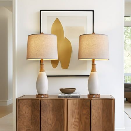 two lamps sitting on top of a wooden cabinet in front of a wall mounted painting