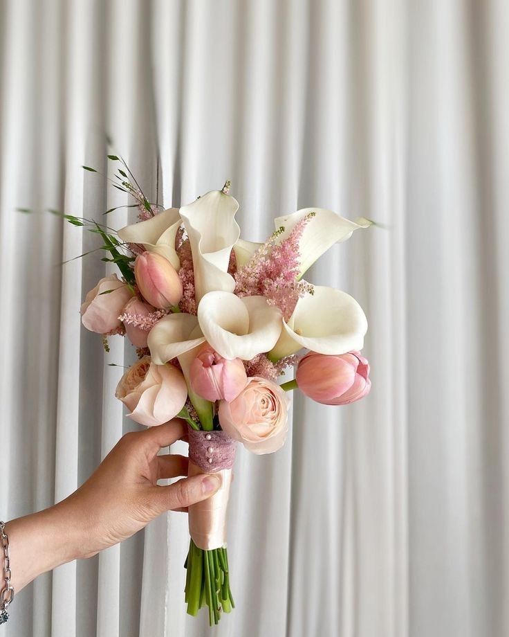 a person holding a bouquet of flowers in front of a white curtained wall with curtains behind it