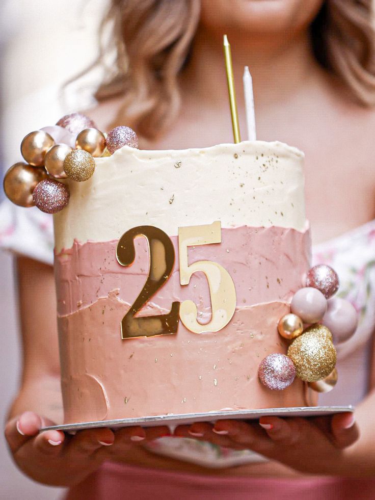 a woman holding a cake with the number twenty five on it