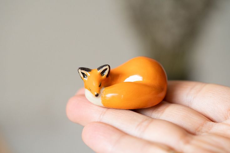 a tiny toy fox sitting on top of someone's hand