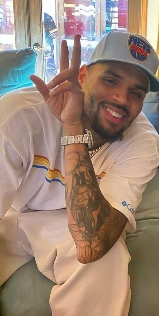 a man sitting on top of a couch making the peace sign with his hand and wearing a hat