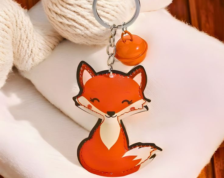 a red fox keychain sitting on top of a white pillow next to a ball of yarn