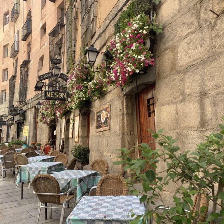 tables and chairs are lined up on the side of an alleyway with flowers hanging over them