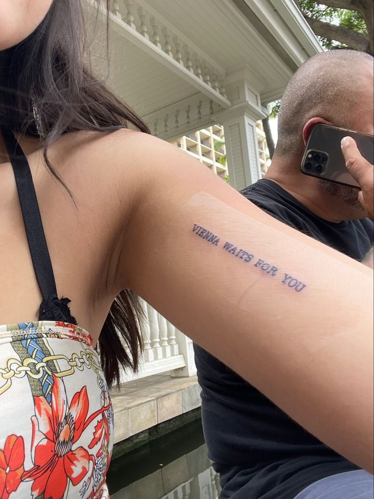 a woman with a small tattoo on her arm next to a man holding a cell phone