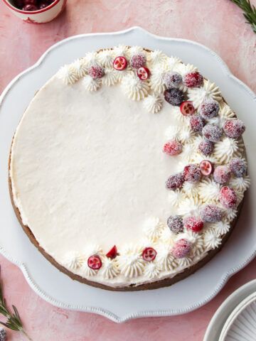 a cake with white frosting and cranberries on it sitting on a table