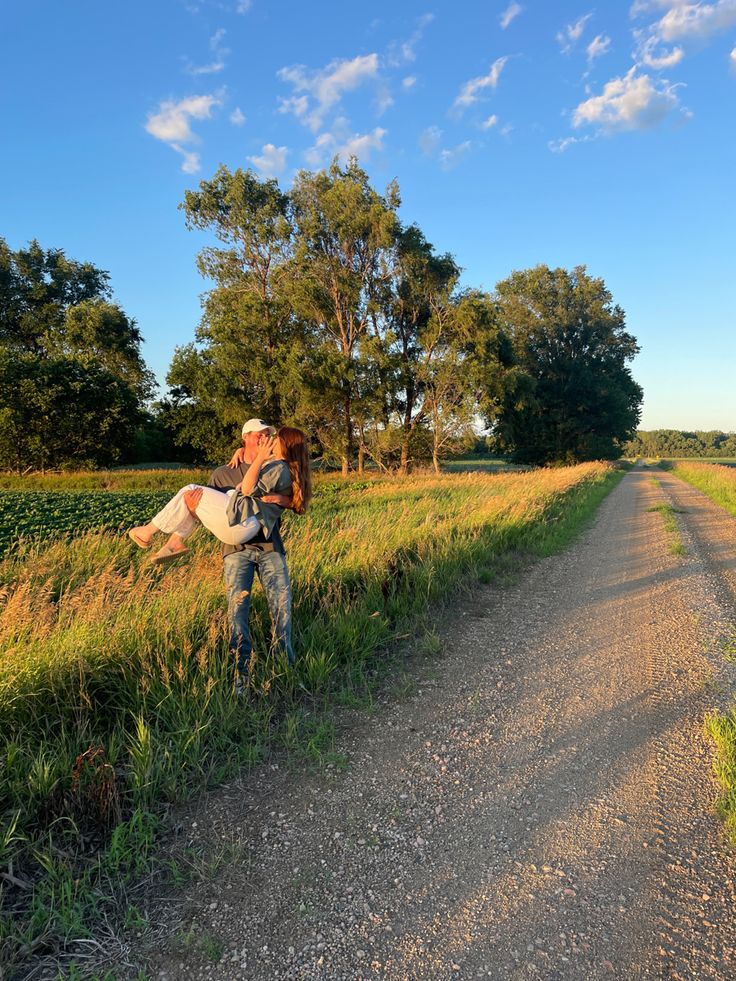 a man carrying a baby on his back walking down a dirt road in the middle of a field