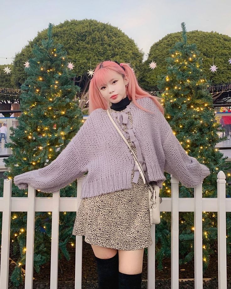 a woman with pink hair and boots standing next to a white fence in front of a christmas tree