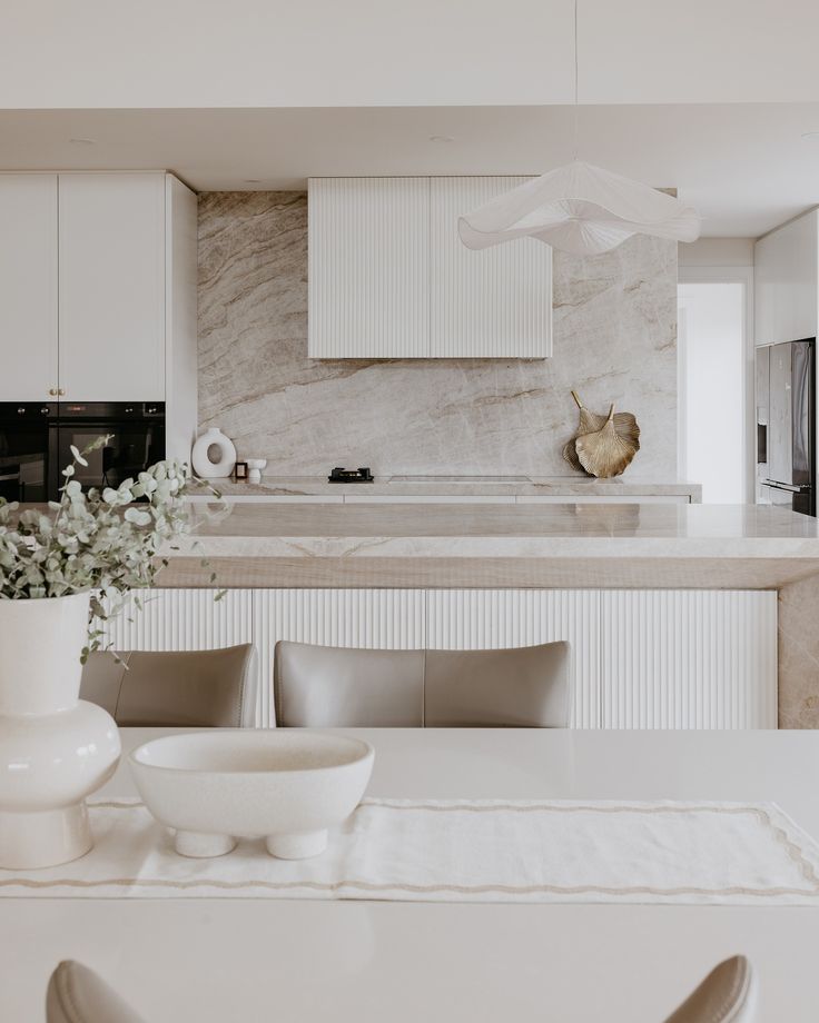 a kitchen with white cabinets and marble counter tops, along with a dining room table set for four