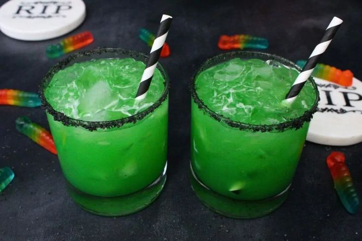 two glasses filled with green liquid on top of a black table next to candy canes