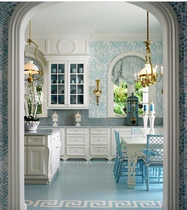 a kitchen with blue and white wallpaper, gold chandeliers, and an archway leading to the dining room