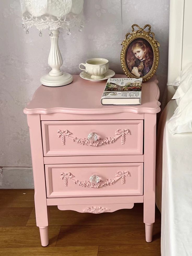 a pink dresser with pictures on it and a white lamp next to the nightstand in the room