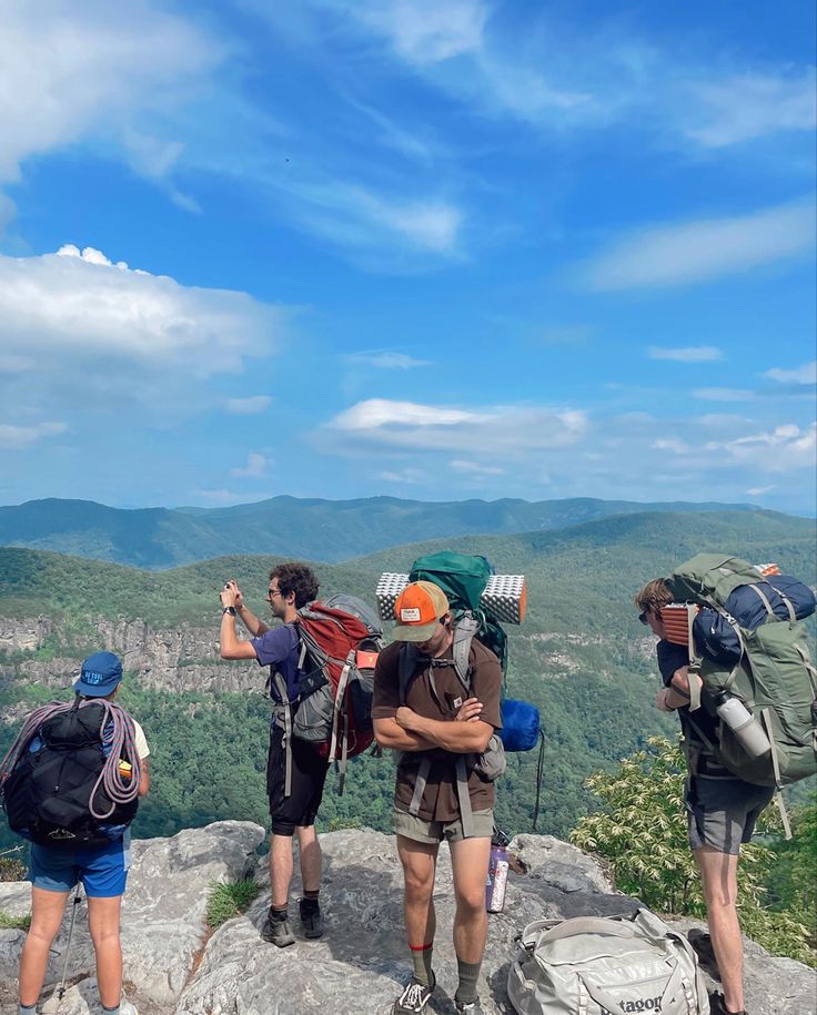 three people standing on top of a mountain with backpacks