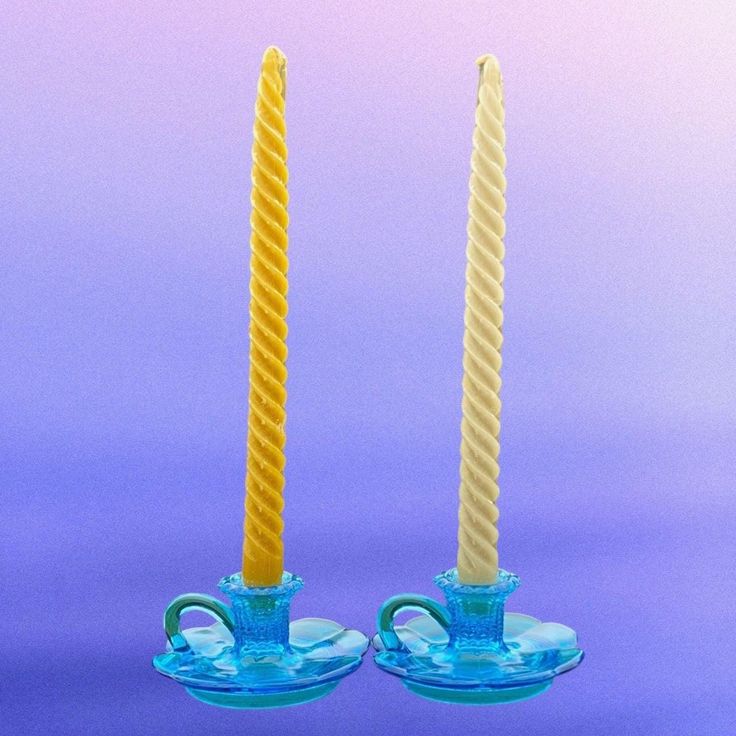 two yellow candles sitting next to each other on top of a blue glass tablecloth