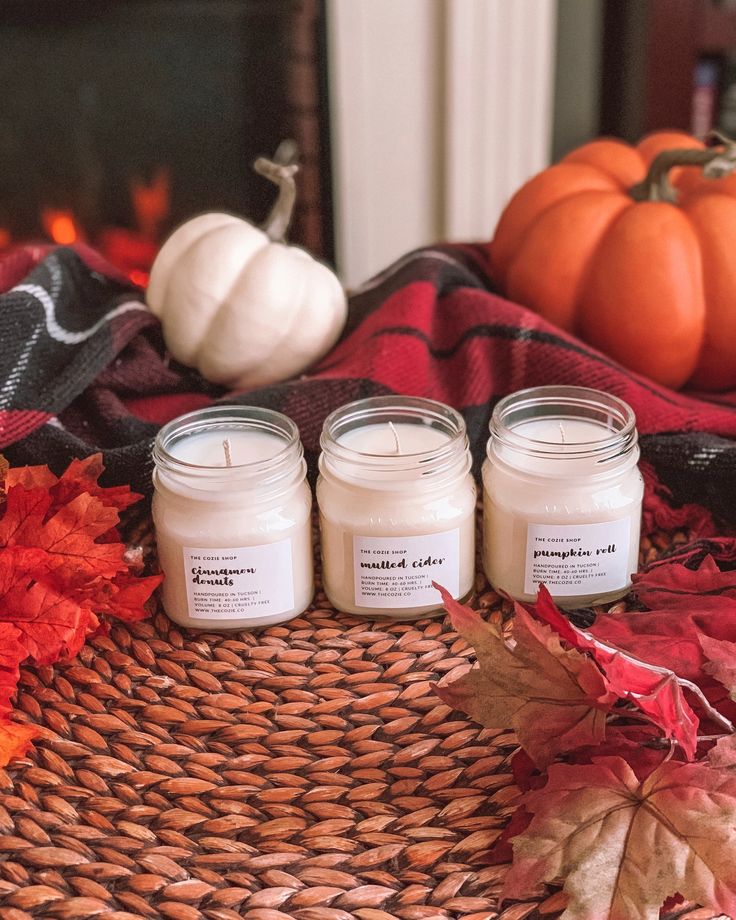 three candles sitting on top of a woven basket next to autumn leaves and pumpkins