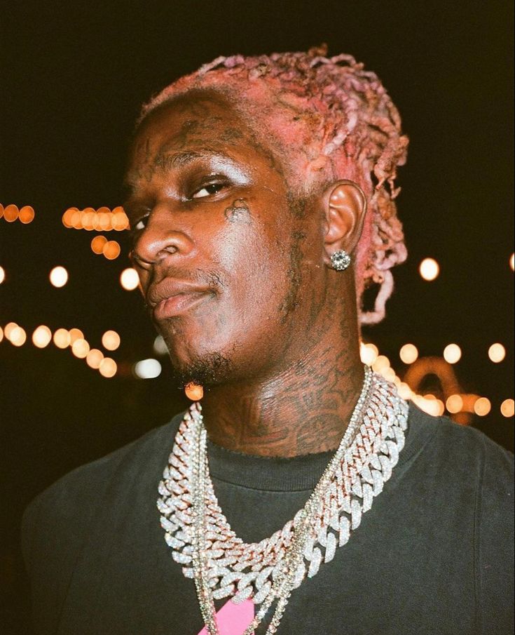 a man with pink dreadlocks wearing a black t - shirt and some necklaces