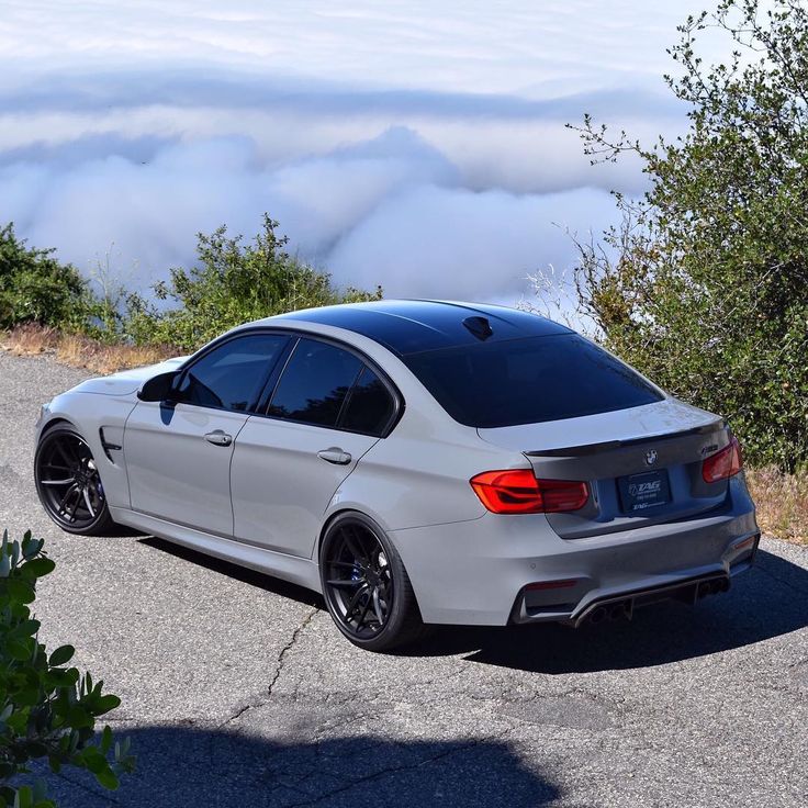 the white car is parked on the side of the road near some bushes and trees