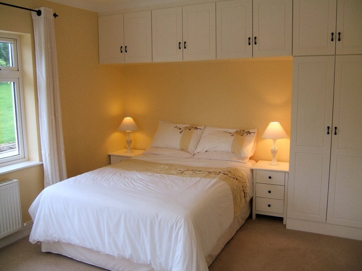 a white bed sitting next to two lamps on either side of a window in a bedroom