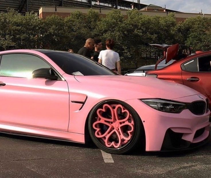 a pink car parked next to other cars in a parking lot with people looking at it