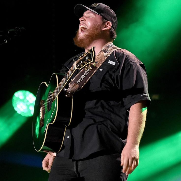 a man holding a guitar on top of a stage with green lights in the background