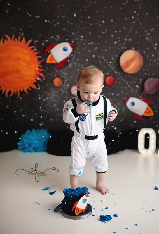 a baby boy standing on top of a cake in front of a space themed backdrop