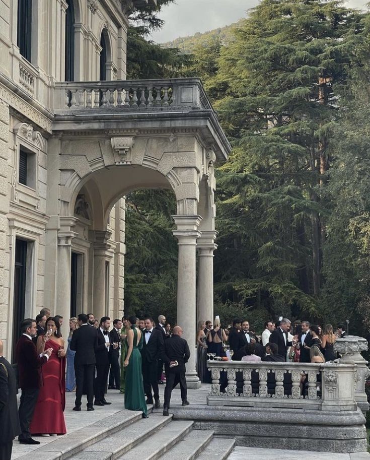 a group of people in formal wear standing on the steps of a large building with columns