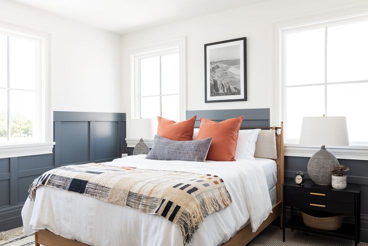 a bedroom with two windows and a bed in the middle, along with pillows on top of it