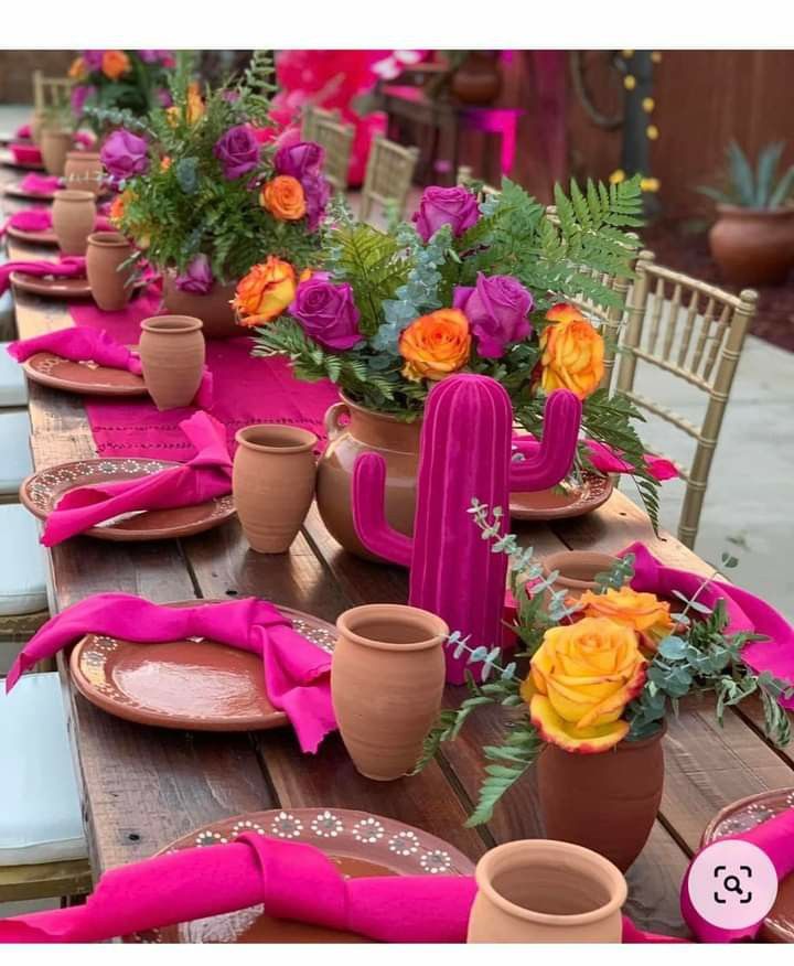 the table is set with pink napkins and cactus plant vases on it, along with other place settings