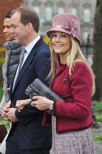 a man in a suit and tie walking next to a woman wearing a pink hat