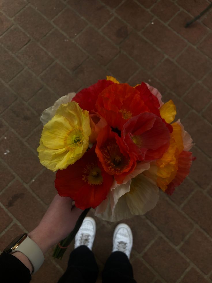 a person holding a bouquet of flowers in their hand on the ground next to a brick wall