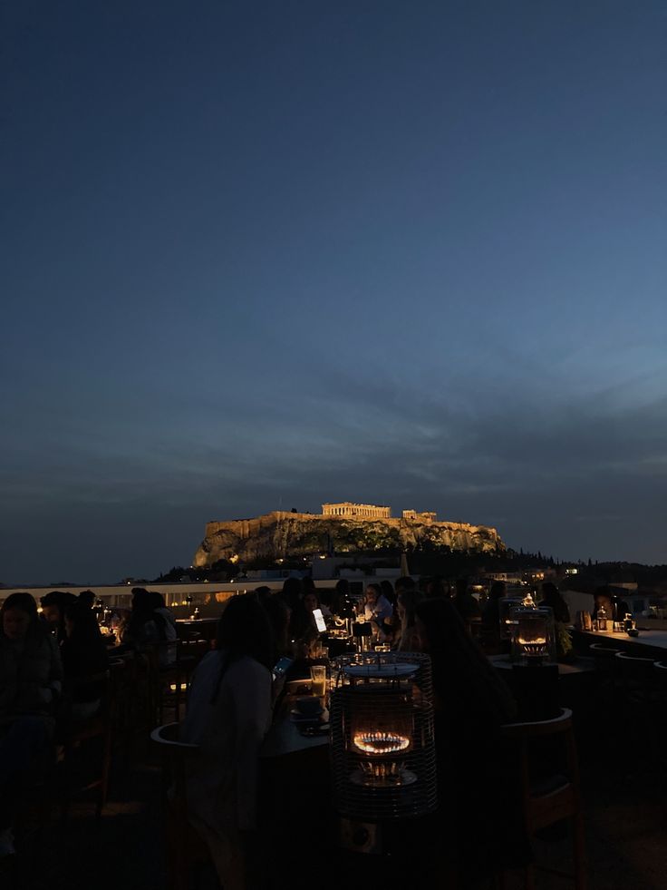 people are sitting at tables in front of the acrobatic castle on top of a hill