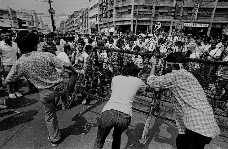 several people standing on the sidewalk near a fence