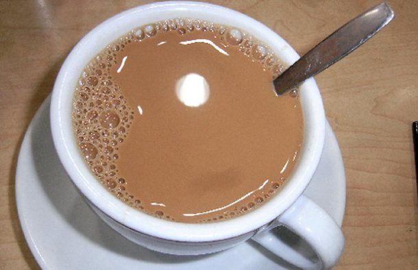 a cup of coffee with a spoon in it on a saucer next to a cell phone