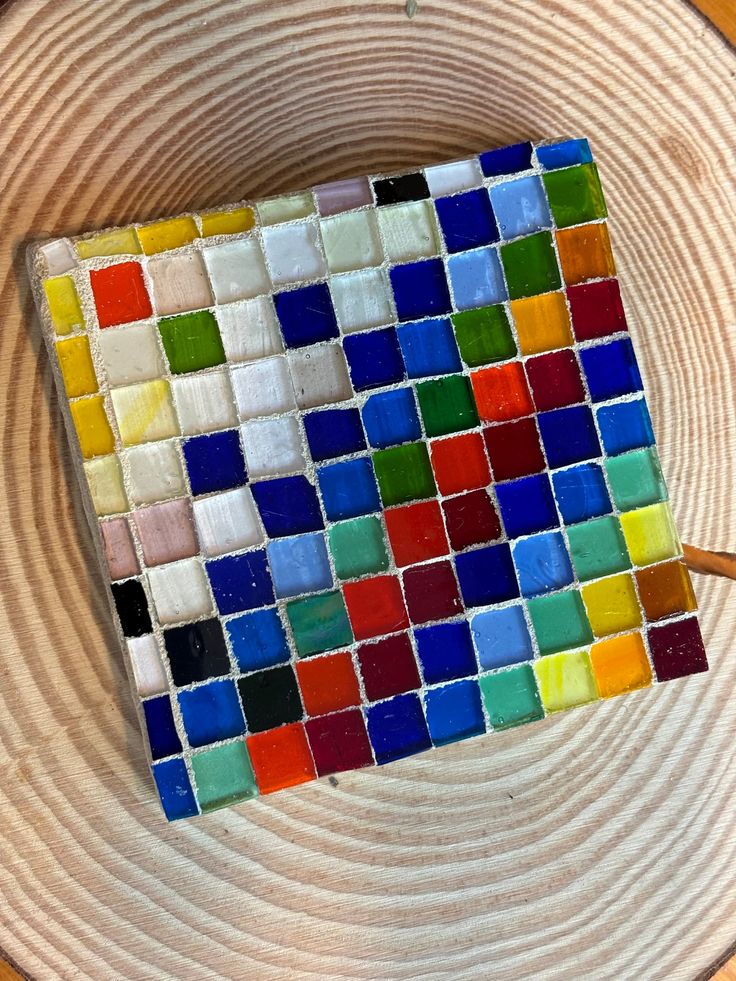 a piece of art made out of colored glass tiles on a wooden surface with a pair of scissors