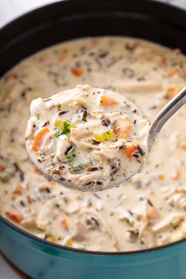 a ladle full of creamy chicken and wild rice soup is being held by a spoon