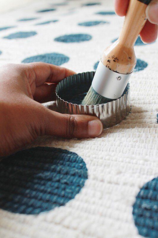 someone using a brush to paint the inside of a cupcake tin on a polka dot tablecloth