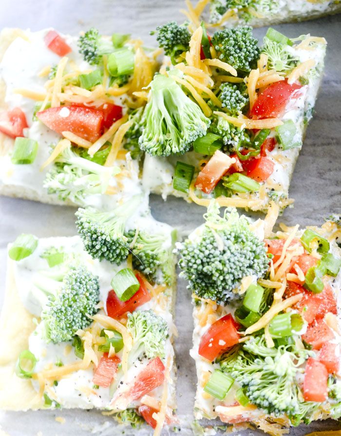 broccoli, tomatoes, cheese and other toppings are arranged on top of square pieces of pizza