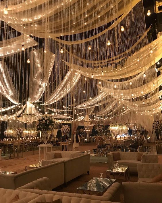 a room filled with lots of white couches and lights hanging from the ceiling above