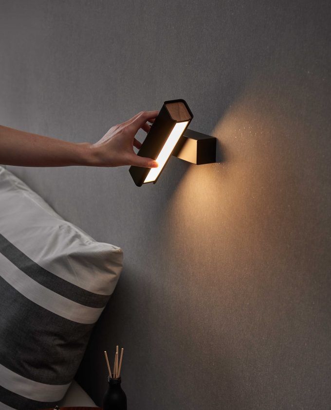 a person's hand is touching the wall light that is on top of a bed