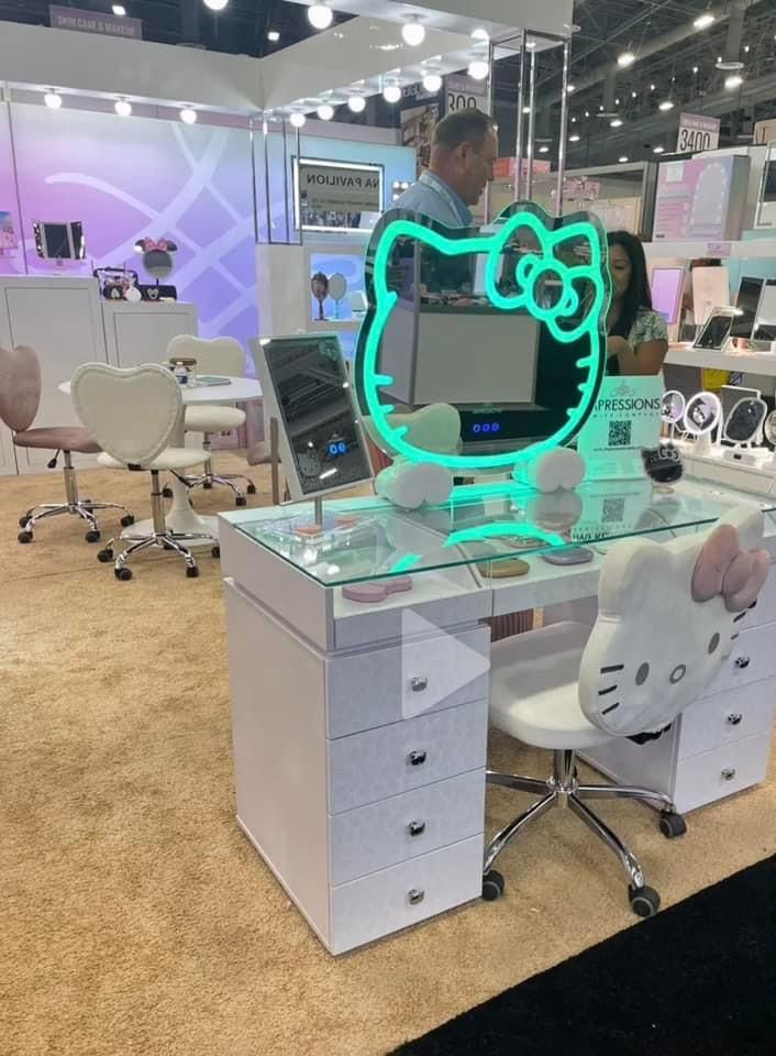 an office desk with a hello kitty mirror on it's top and two people looking at the screen