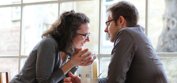 a man and woman sitting at a table talking to each other in front of a window