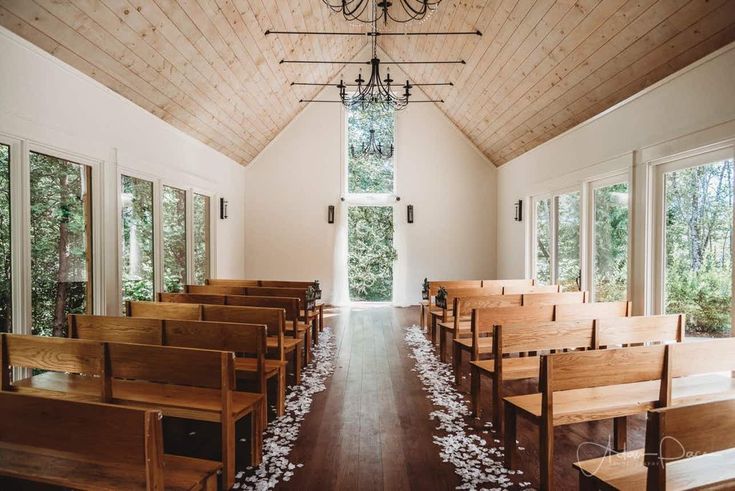 an empty church with wooden pews and white petals on the floor in front of windows