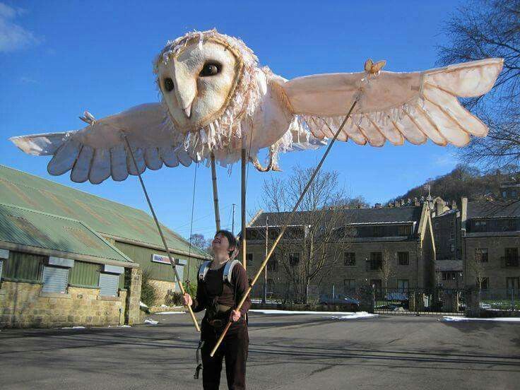 an owl puppet being held by a woman in the middle of a street with buildings behind it