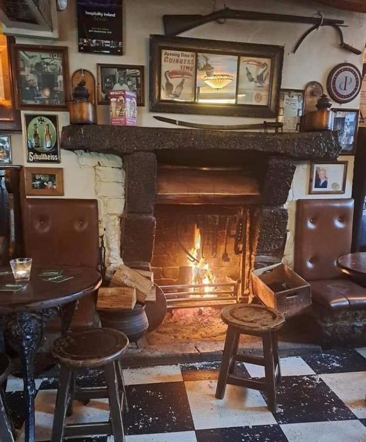 a room with chairs, tables and a fire place in the center is decorated with pictures on the walls