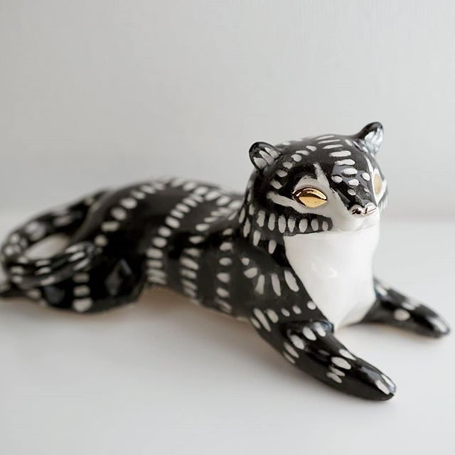 a ceramic black and white cat figurine laying on its side with eyes open