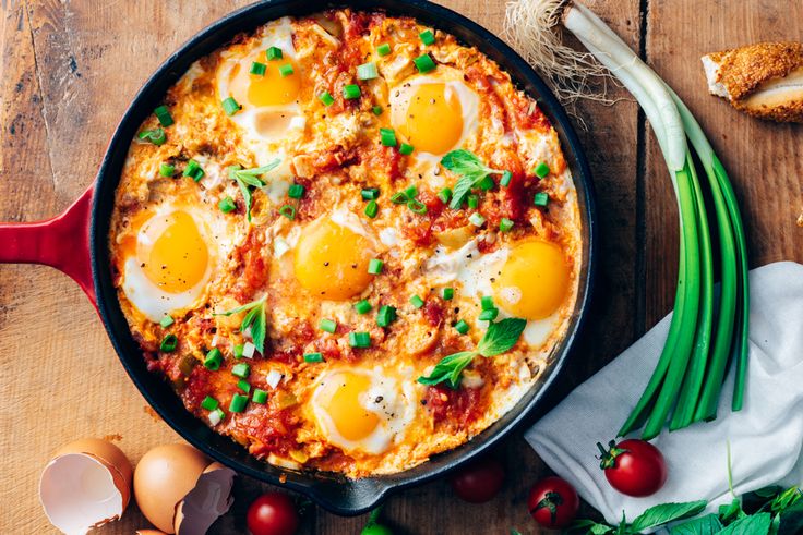 an egg in a skillet with tomatoes, green onions and bread on the side