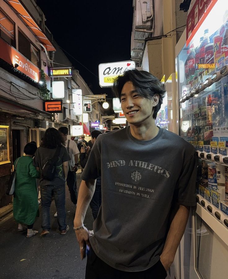 a man standing in front of a store on the side of a street at night