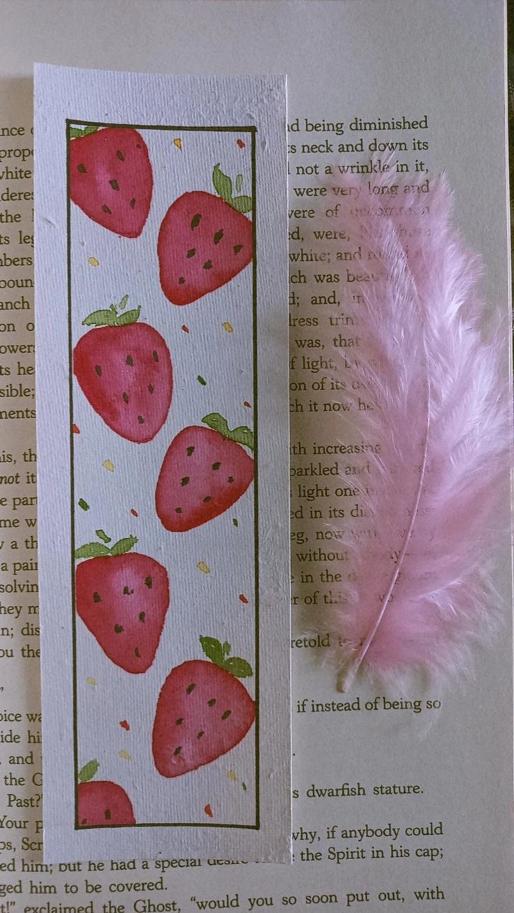 a bookmark with strawberries on it next to a pink feather