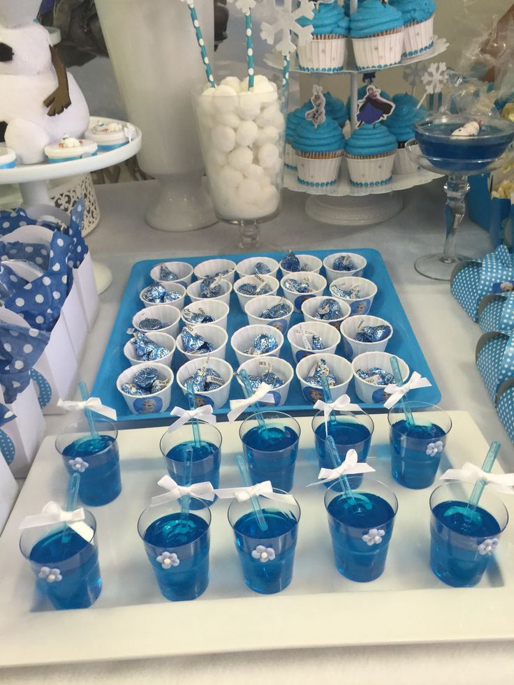 a table topped with cups filled with blue liquid and cupcakes on top of it